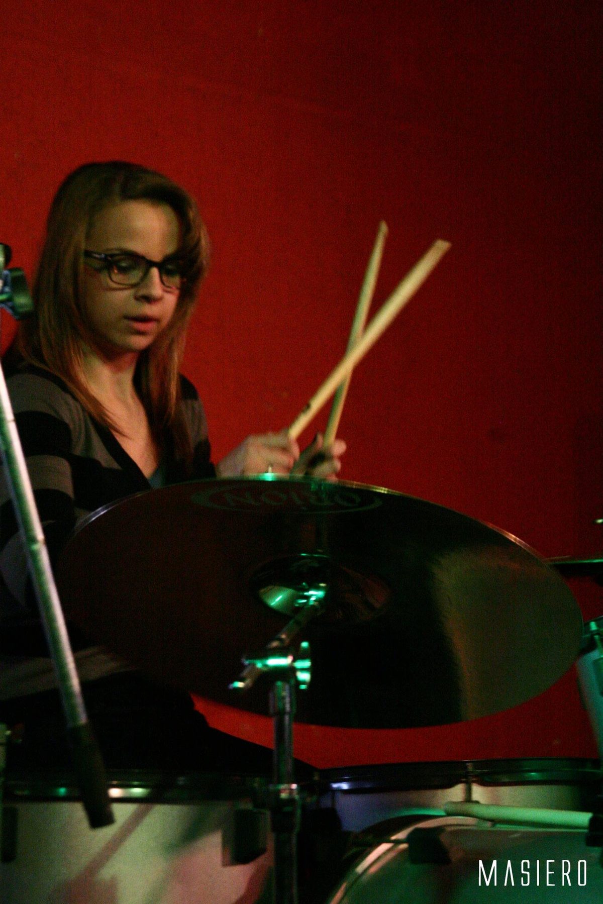 Baterista de óculos tocando sob luz vermelha.