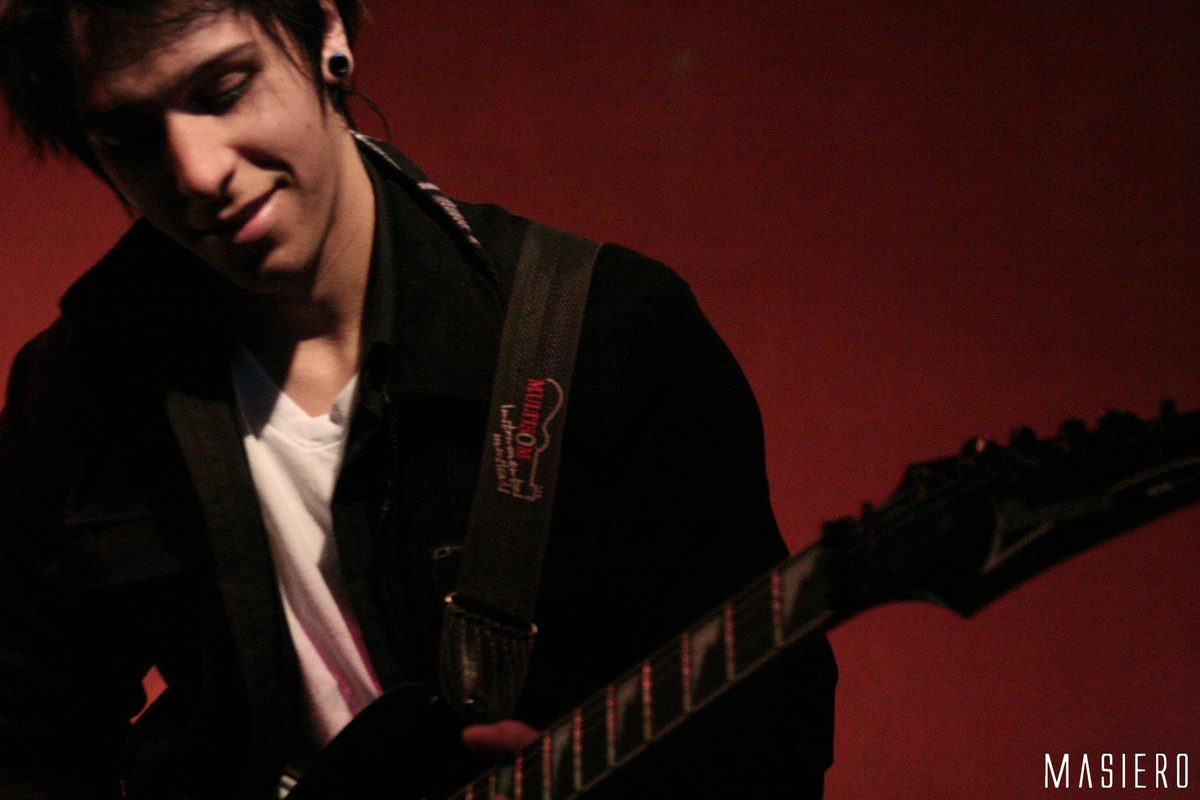Guitarrista sorrindo sob luz vermelha, com a guitarra em primeiro plano.