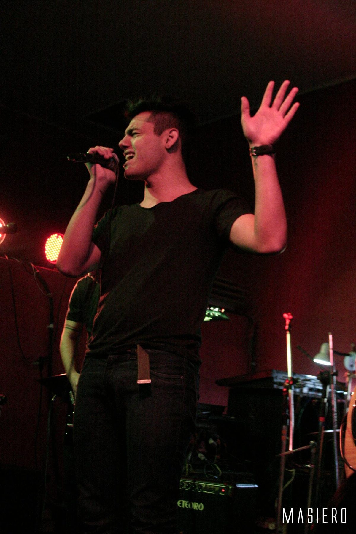 Vocalista de braço erguido no palco, sob luz vermelha. Foto: Masiero.