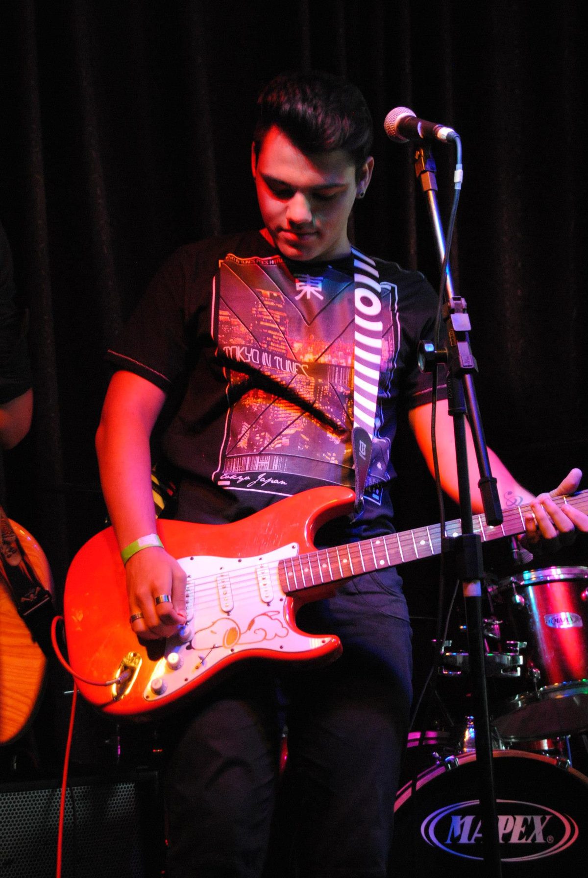 Vocalista tocando guitarra vermelha de cabeça baixa.