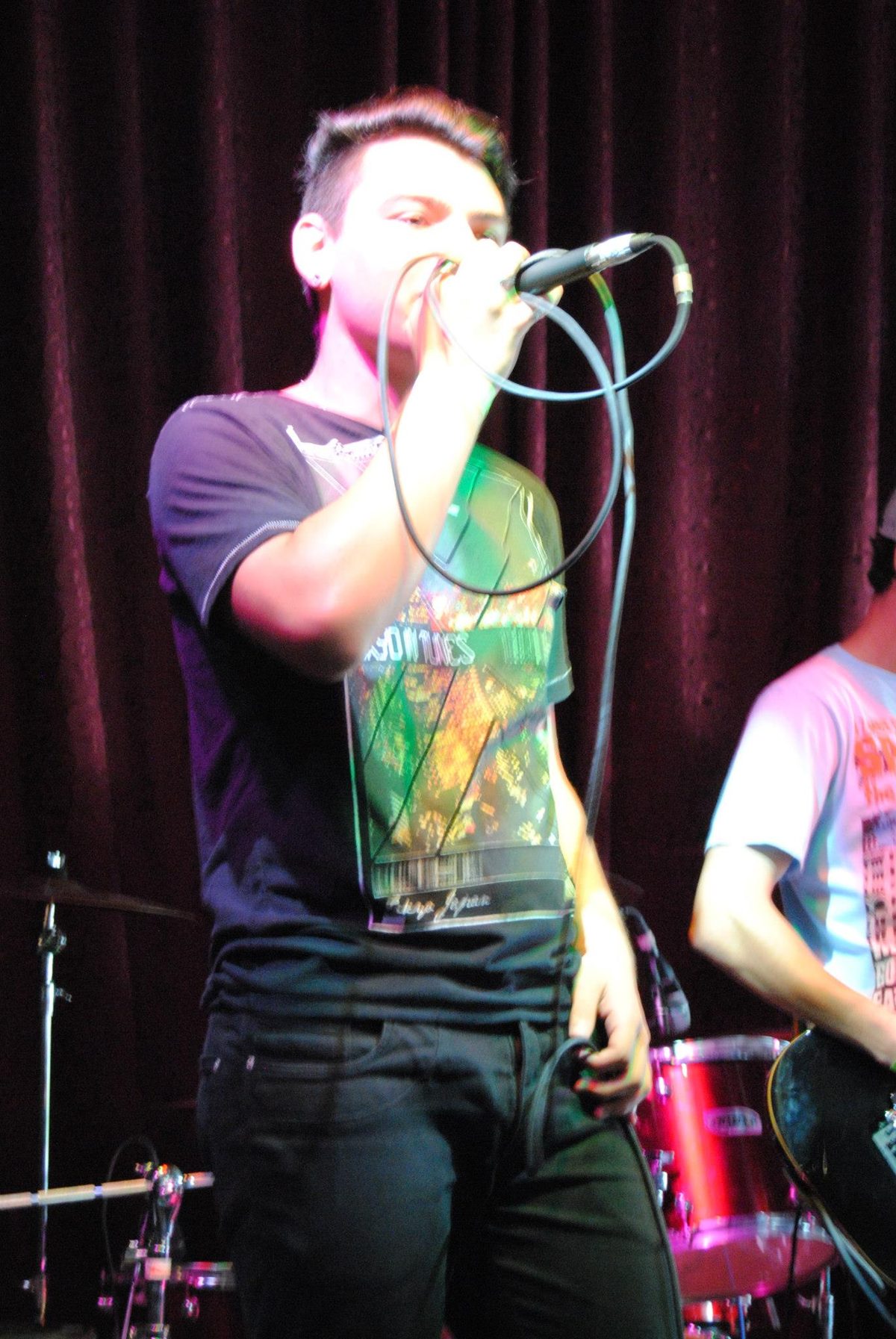 Vocalista cantando ao microfone, de camiseta estampada.