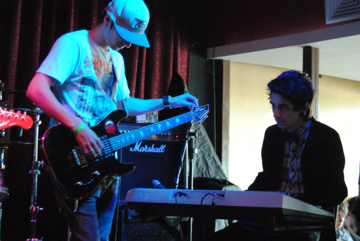 Guitarrista de boné e tecladista no palco.