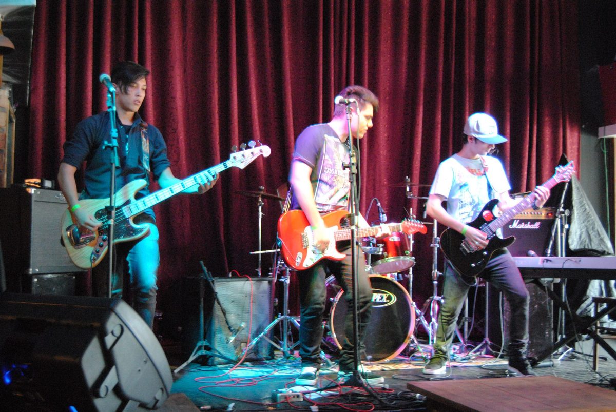 Banda no palco no primeiro show da segunda fase, cortina vinho ao fundo.