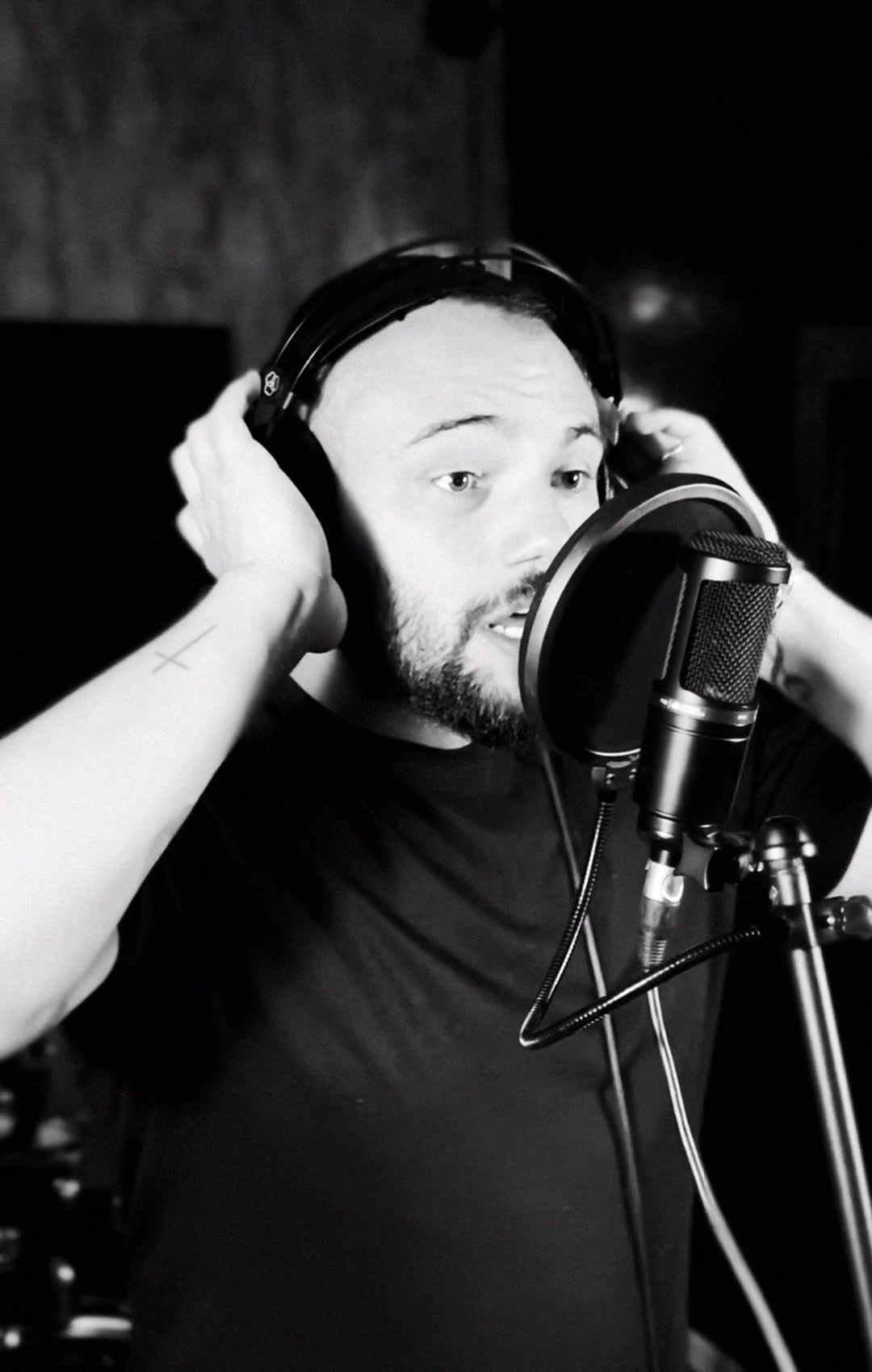Matheus de perfil ajusta o fone enquanto canta, com o teto acústico do estúdio ao fundo.